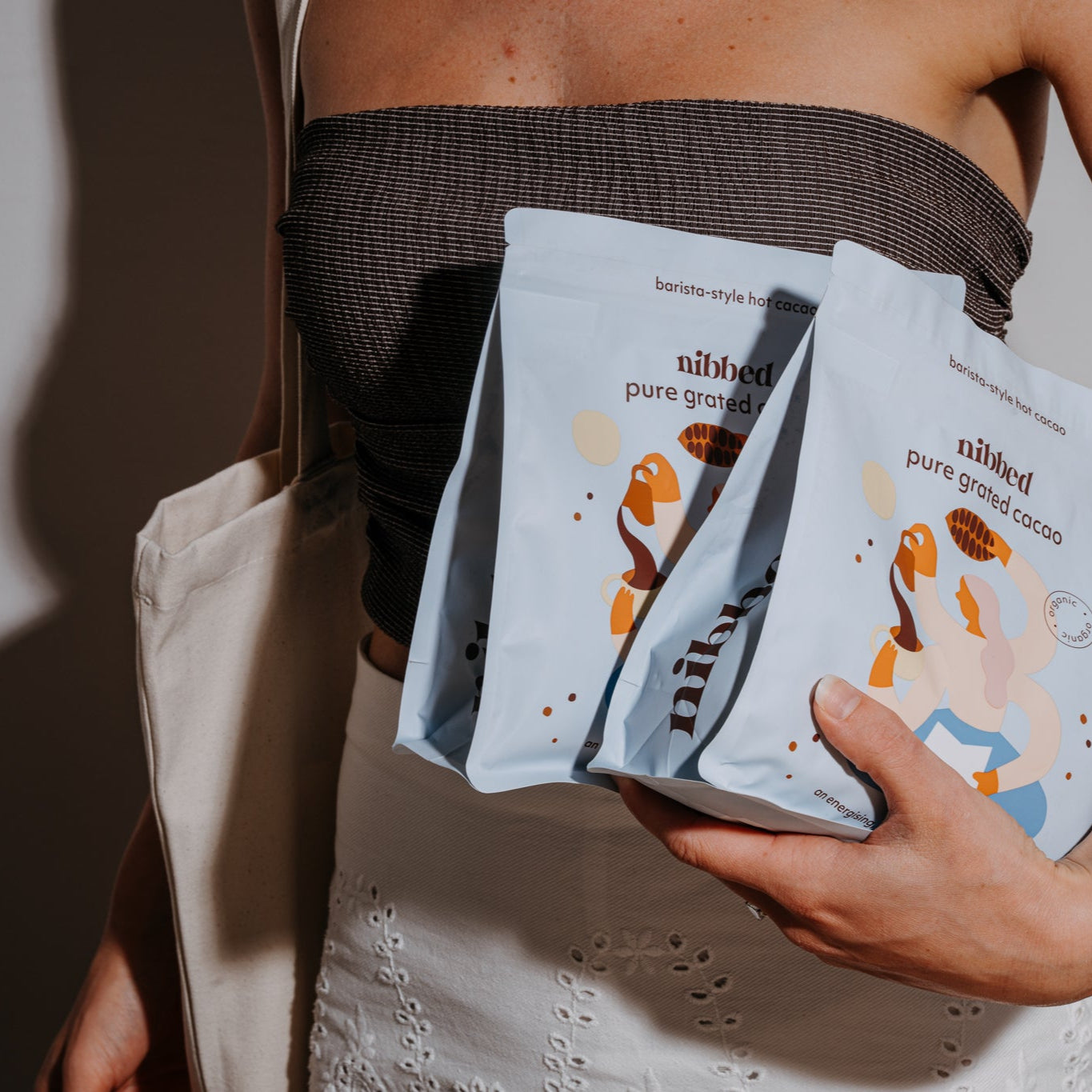 Person holding multiple 'nibbed' pure ground cacao packages against a neutral background