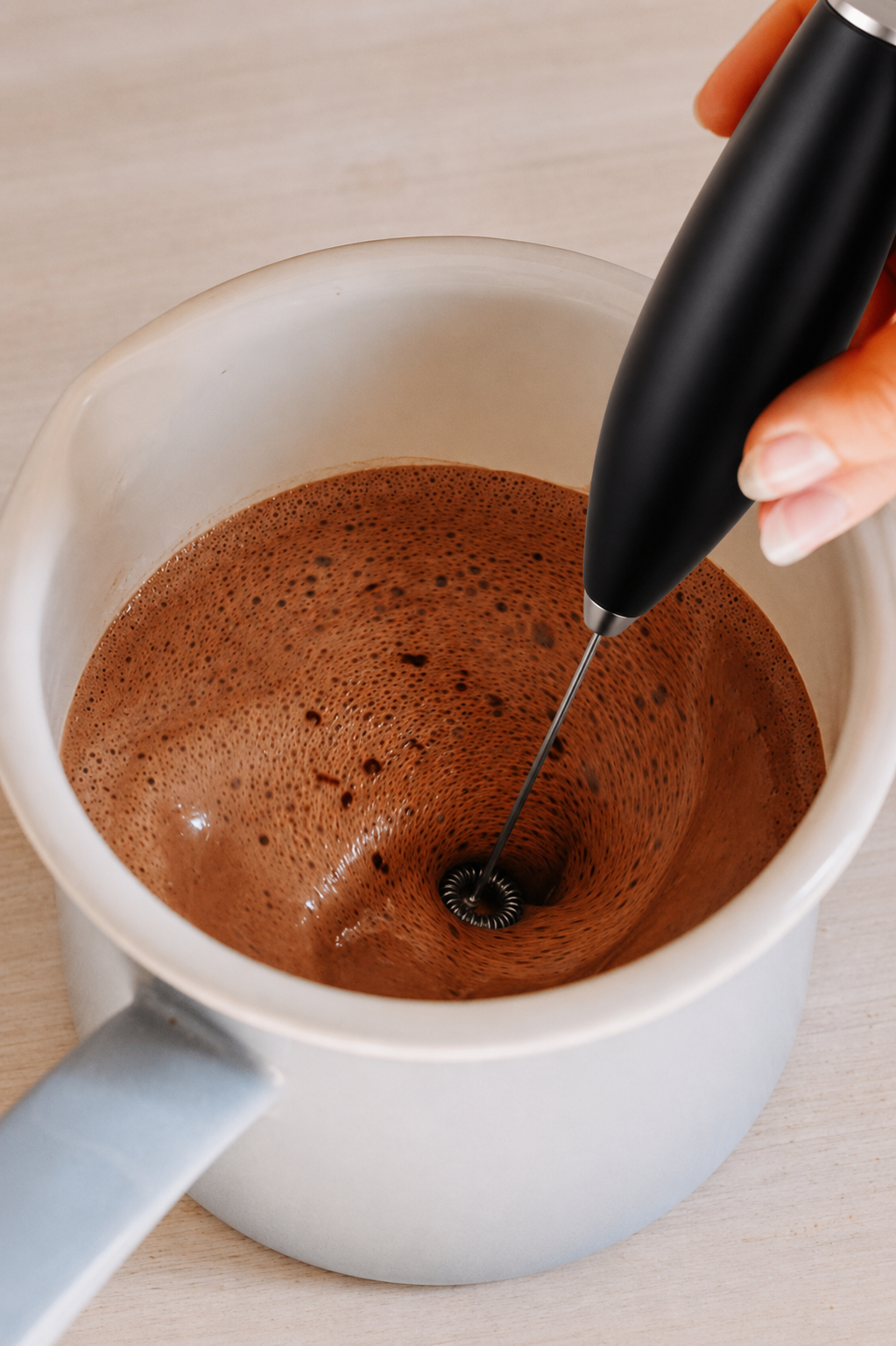 Person using a milk frother to create foam in a mug of hot cacao