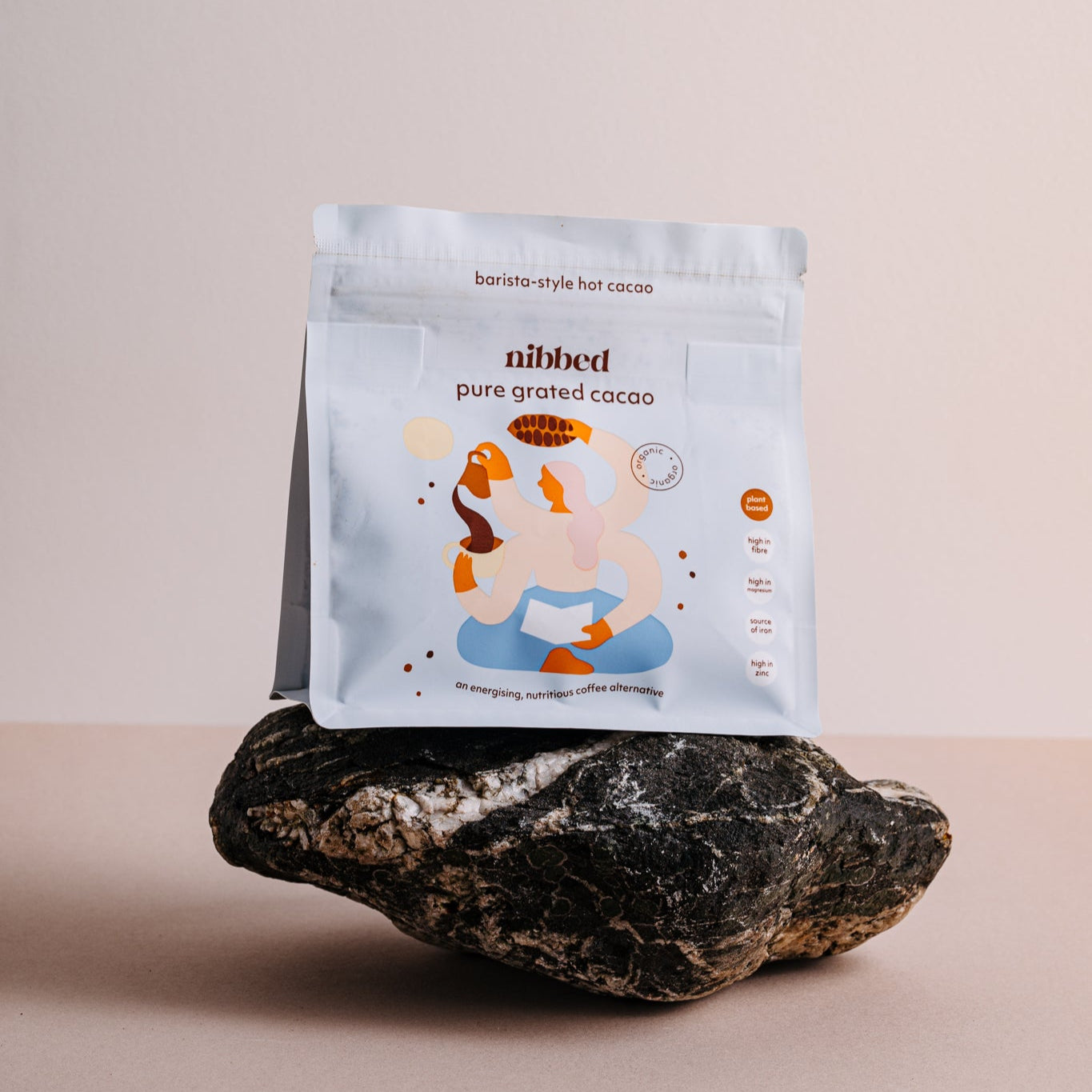 Nibbed pure ground cacao package on a rock with a beige background